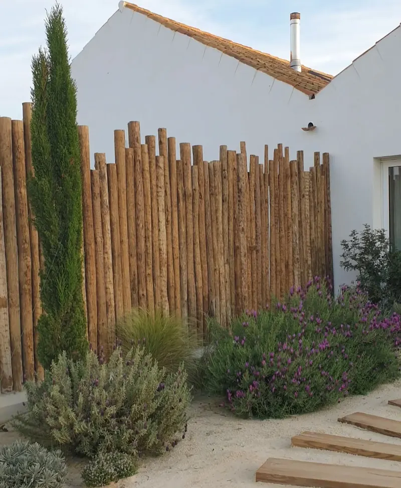 Cerramiento de palos de eucalipto en el jardín de una casa blanca